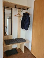 Helle Garderobe aus Echtholz mit einem großen Spiegel, Kleiderbügeln, zwei grauen Sitzkissen auf einer Bank und einer Schuhablage auf Holzboden.