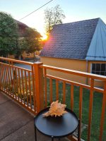 Eine große Deko-Muschel liegt auf einem kleinen schwarzen Beistelltisch auf dem Balkon im warmen Licht des Sonnenuntergangs.