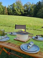 Gartentisch mit einem kompakten Tischgrill und gedecktem Geschirr im Grünen