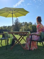 Blick auf einen gemütlichen Gartentisch mit Sonnenschirm und Frau am Waldrand