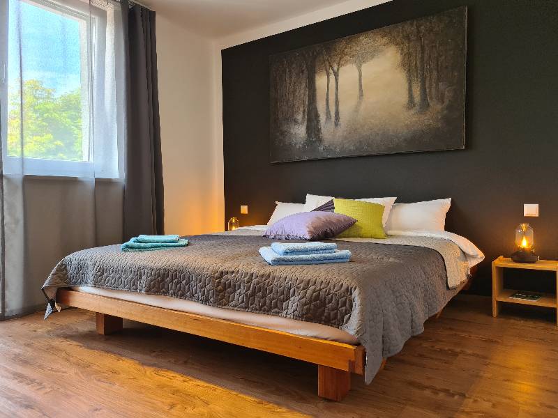 Großes Doppelbett aus Holz im stilvollen Hauptschlafzimmer der Ferienwohnung am Kobernaußerwald im Innviertel.